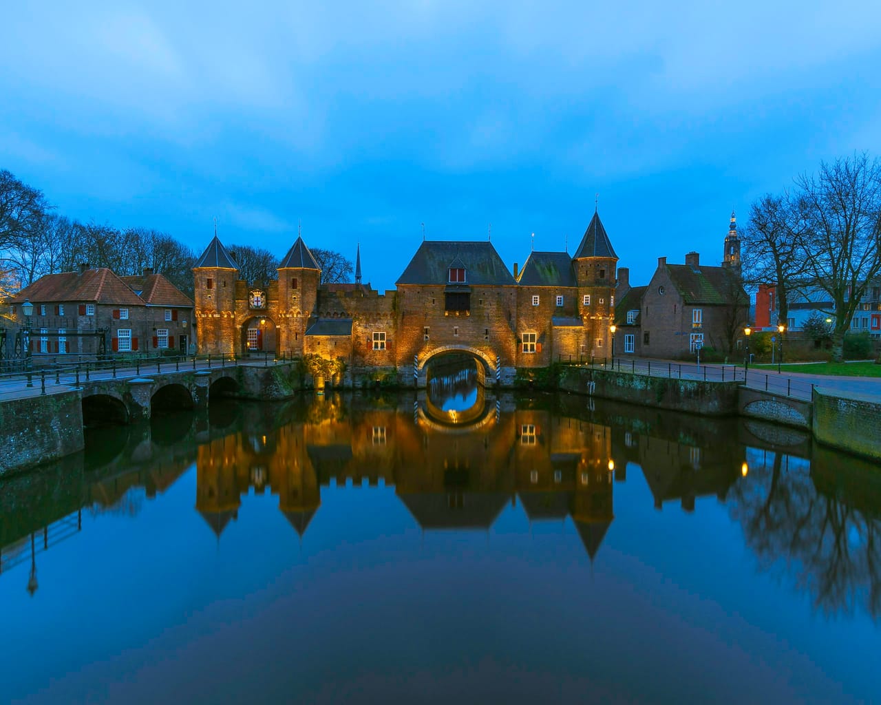 De verlichte Koppelpoort bij avond, weerspiegeld in het water